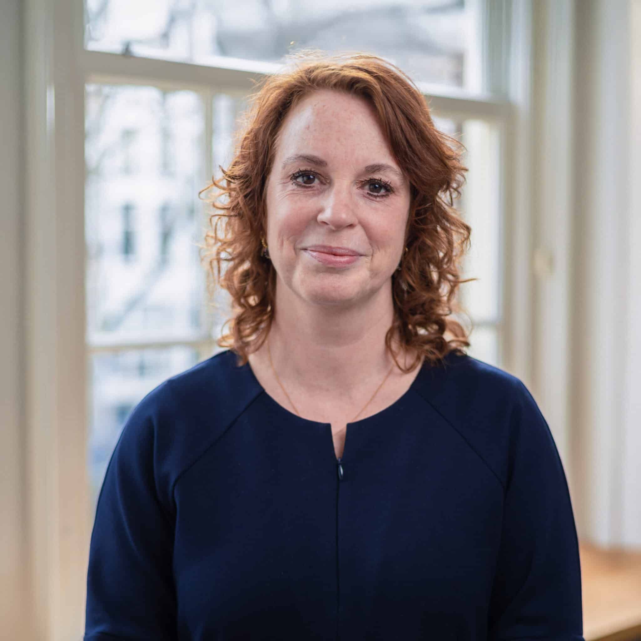 Zakelijk portret van een vrouw met rood haar voor een raam. Bedrijfsportretten Joep van Drunen Photography.